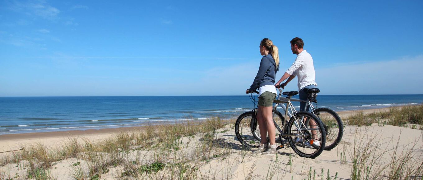 2 E-Bike Fahrer stehen auf einer Sanddüne und schauen aufs Meer